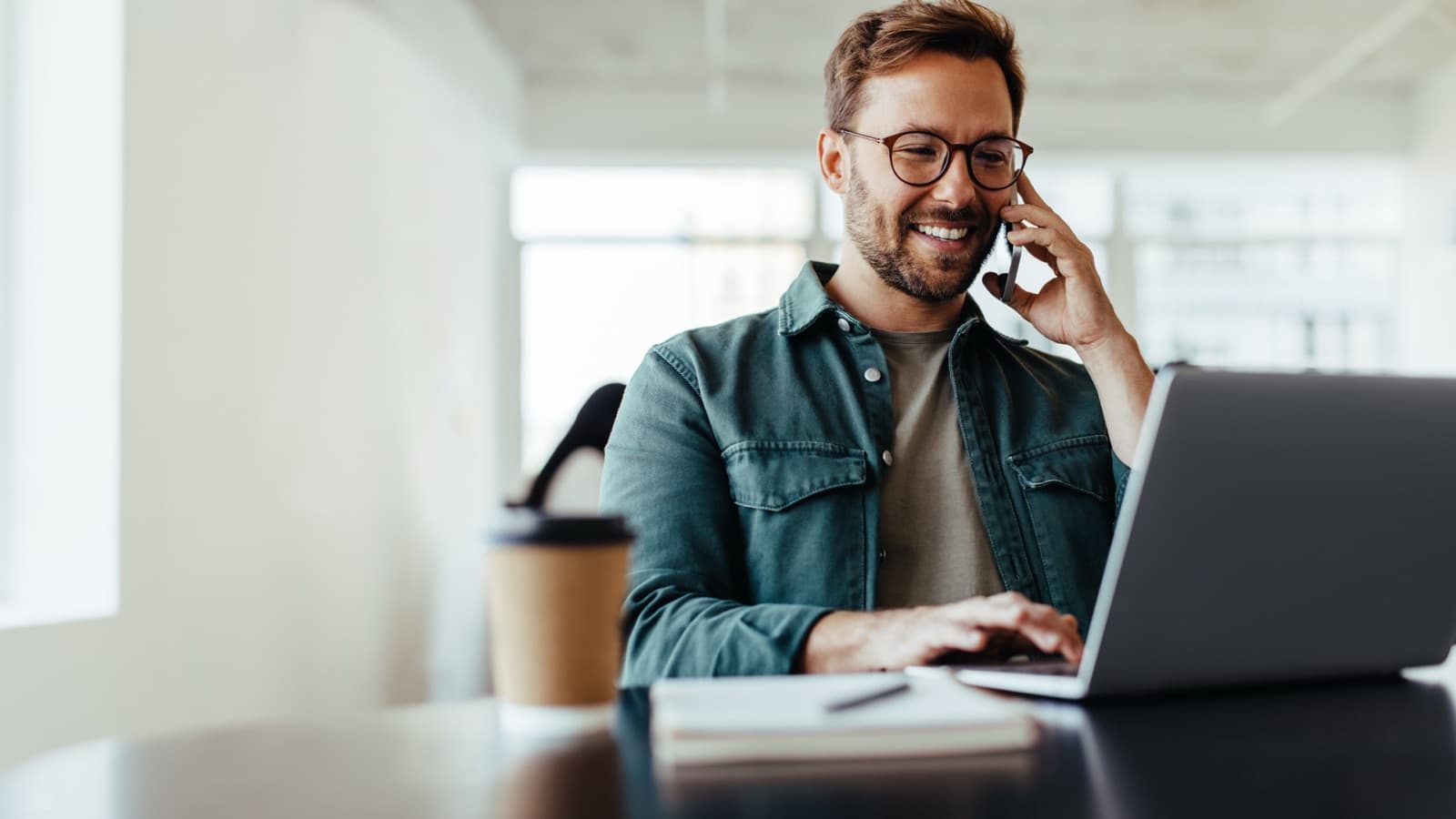 Homme au téléphone devant son ordinateur portable, qui échange avec son assureur